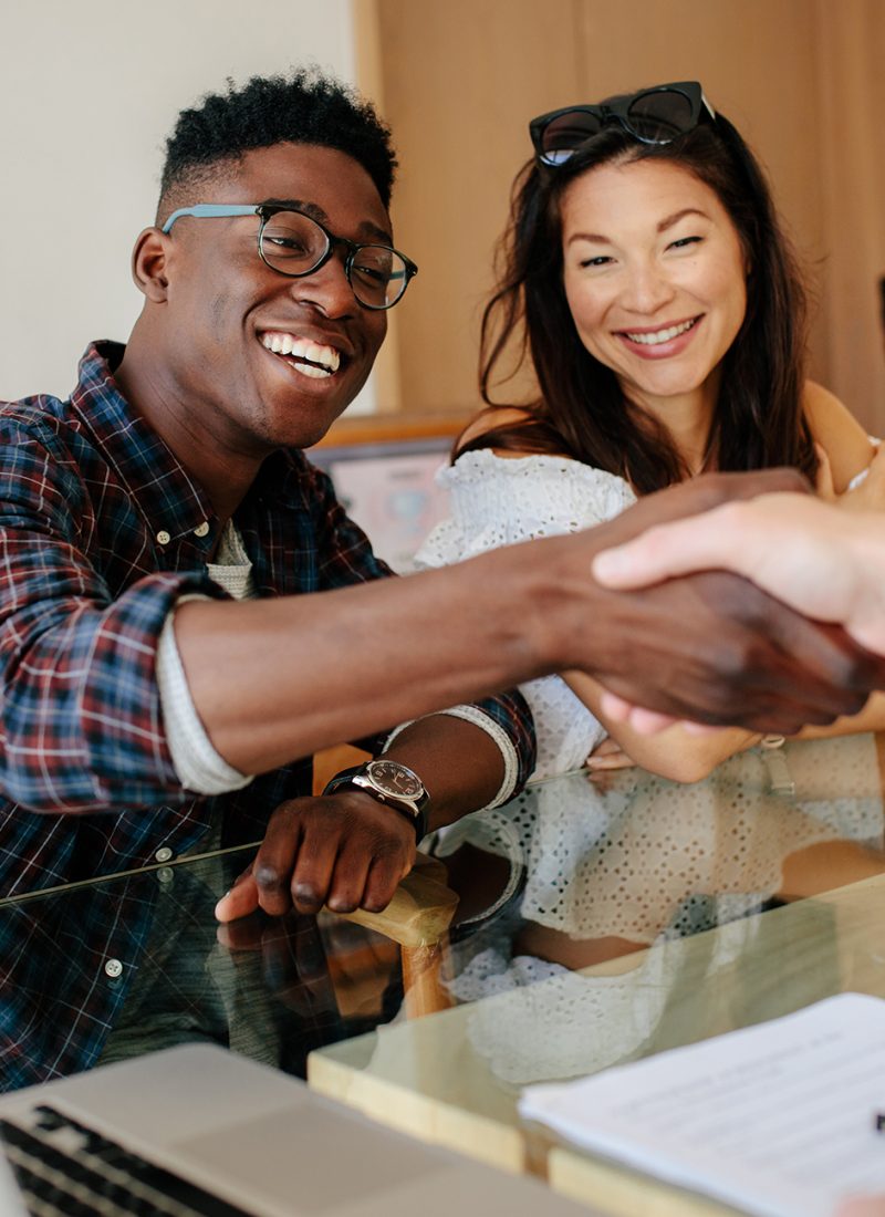 Happy property owners shaking hands with real estate broker after a deal. Young couple handshaking real estate agent after signing contract.